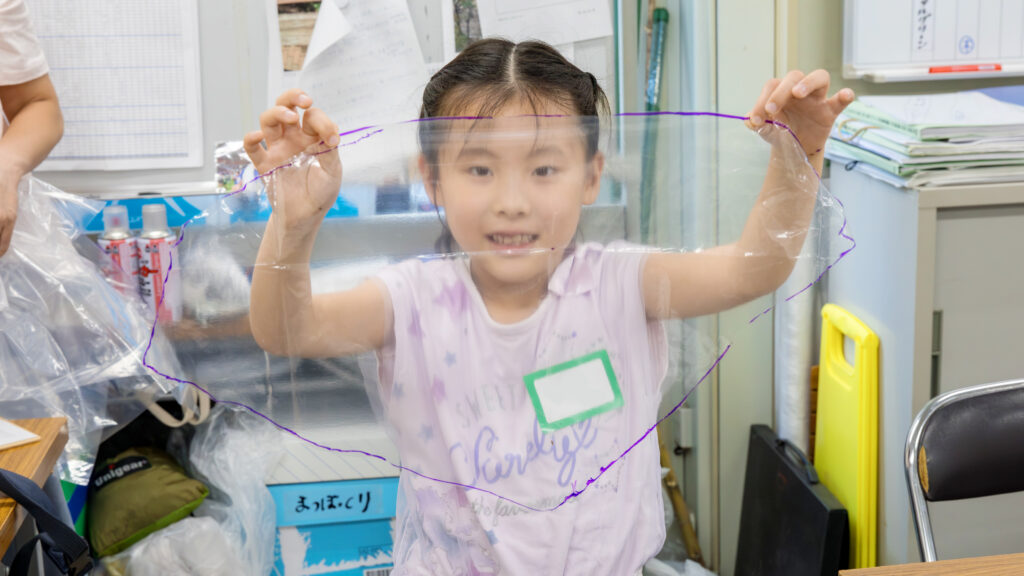 小学生の女の子が自作のビニール製パラシュートを広げるペットボトルロケット教室の様子