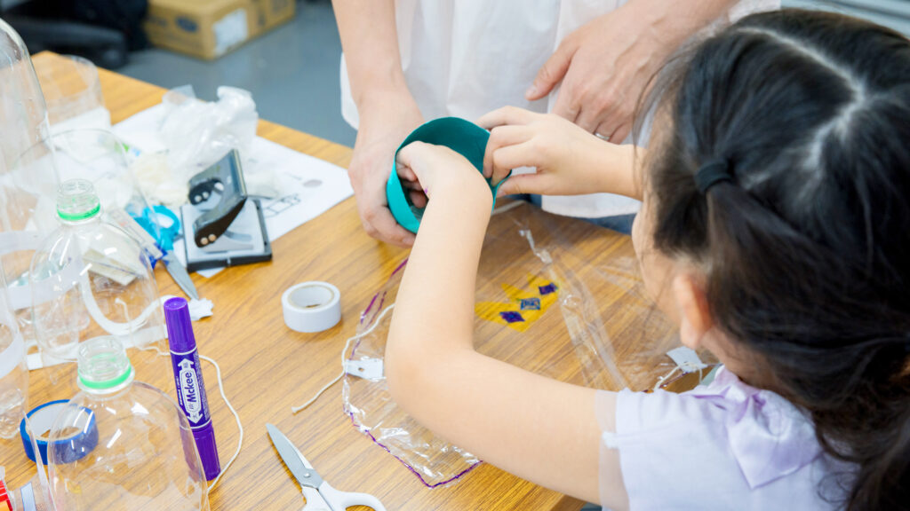小学生が自作のペットボトルロケットにの先に重りを入れている工作の様子