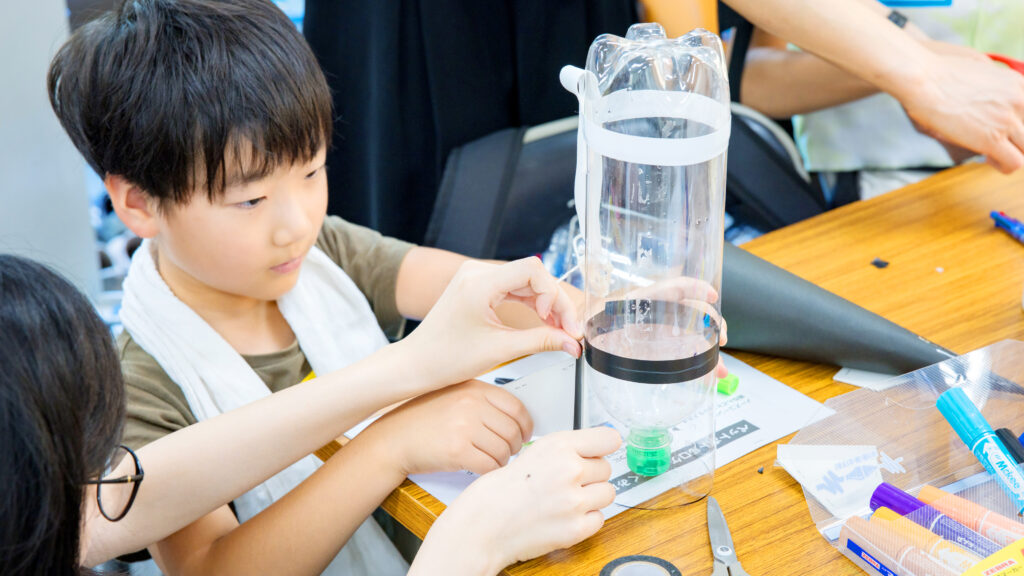 小学生がペットボトルロケットの本体を組み立てる工作中の様子(STEAMイベント)
