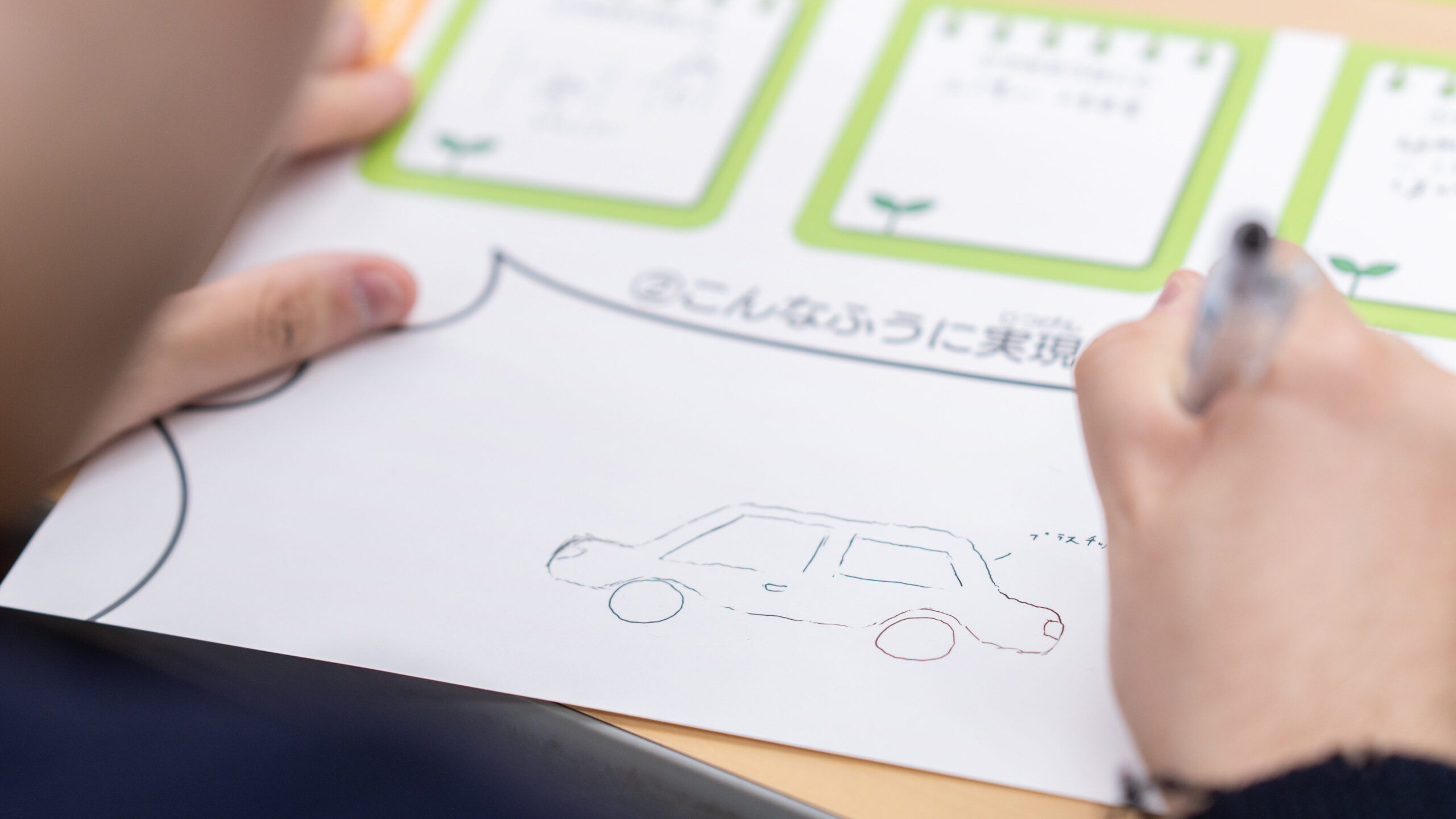 高専生が未来の品川のサステナブル施設をイメージし、ワークシートに車のアイデアスケッチを描く様子。ミッション3の未来施設のデザイン工程。