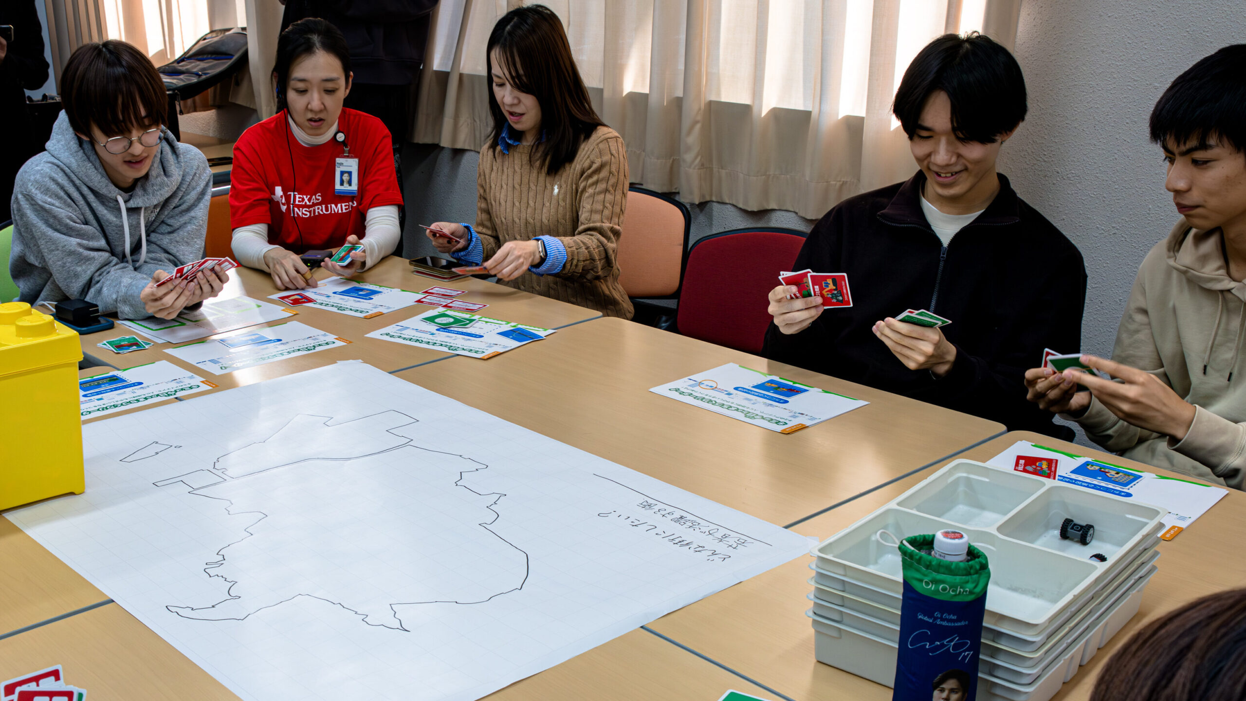 高専生とTI社員が施設・設備カードを確認しながら未来の品川の都市計画を考えるミッション1のワークショップ風景。白地図を囲んで議論する様子。