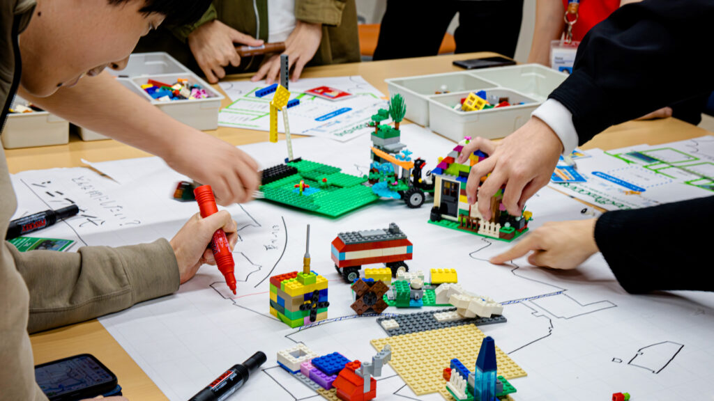 高専生がレゴで制作した未来の品川の施設を白地図上に配置し、サステナブルな都市計画を議論しながら街のレイアウトを描き込むワークショップのシーン。」