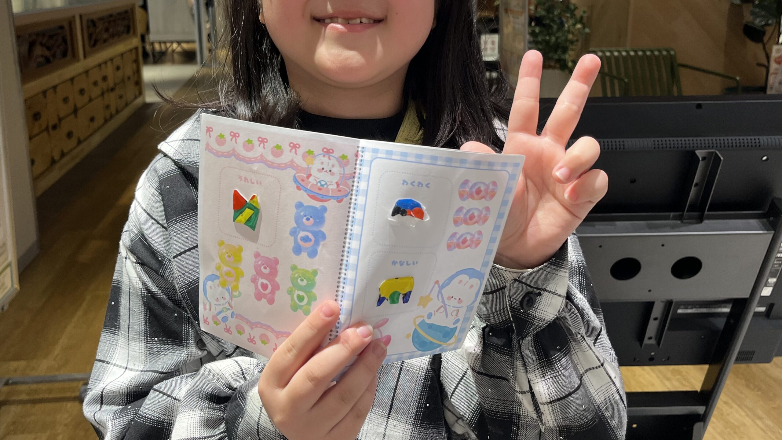 完成したボンボンドロップ風シールを貼ったシール帳を子どもが手に持ち ピースサインで作品を見せている様子