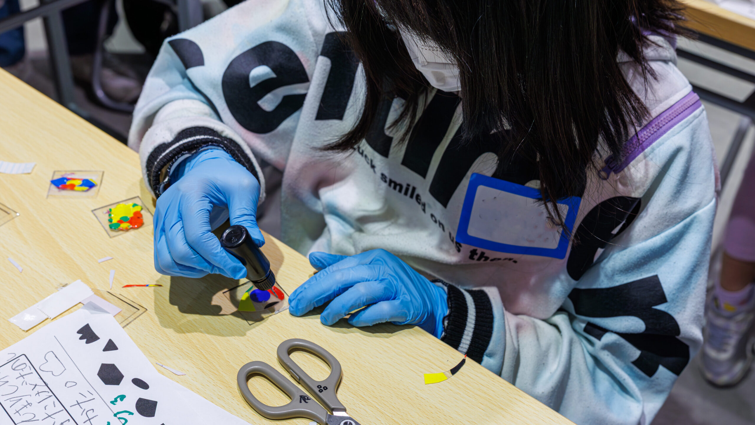 手袋とマスクを着用してUVレジンをシールにのせる作業の様子