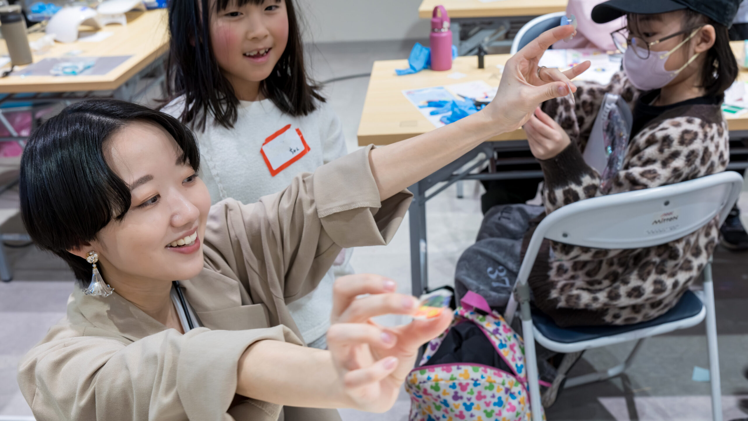 ミッテン府中のワークショップで スタッフが透明なシール素材を手に取り 子どもたちに見せながら作り方を説明している様子