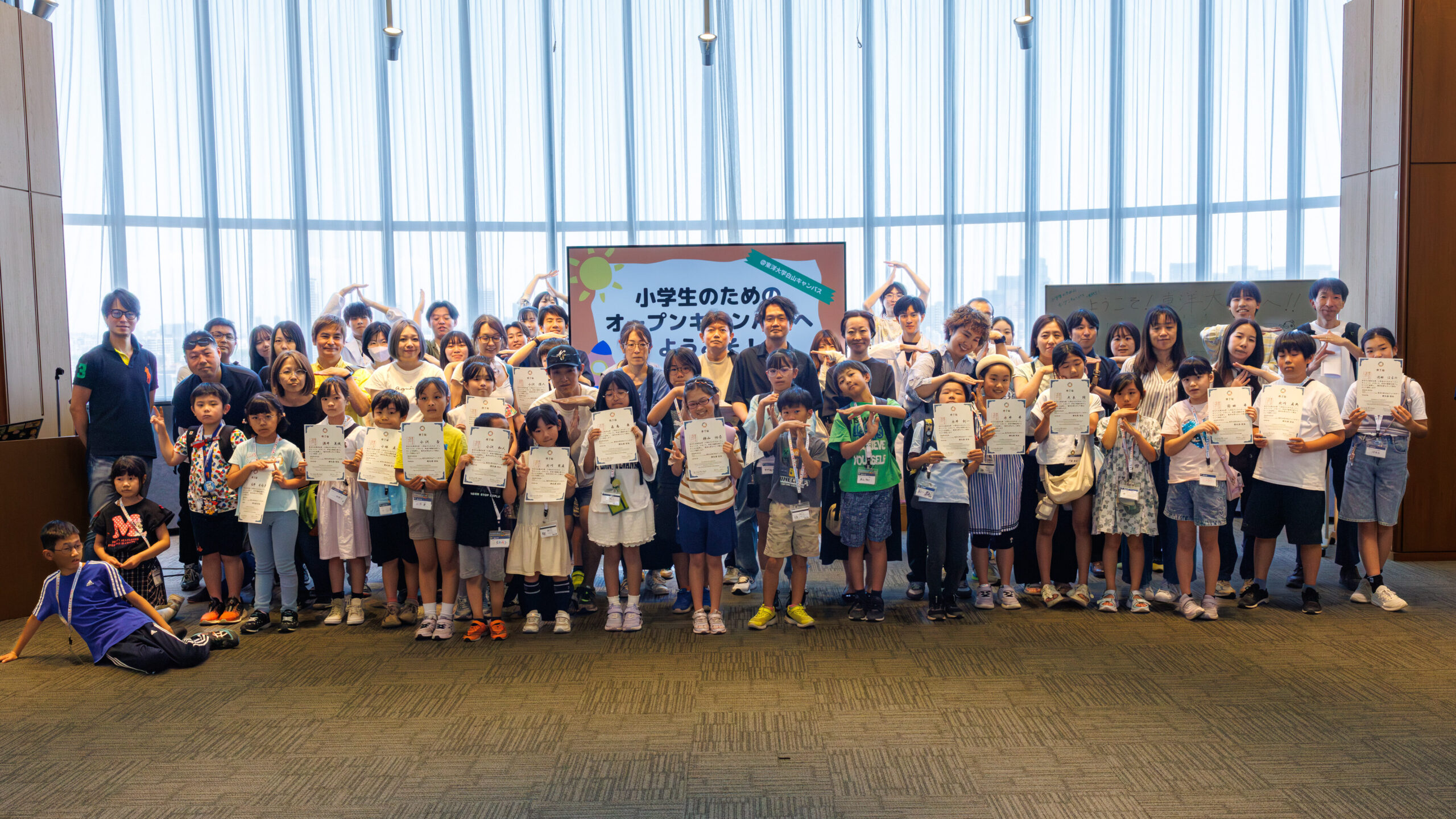 東洋大学白山キャンパスで開催された小学生のためのオープンキャンパスで修了証を手にする参加者とスタッフの集合写真