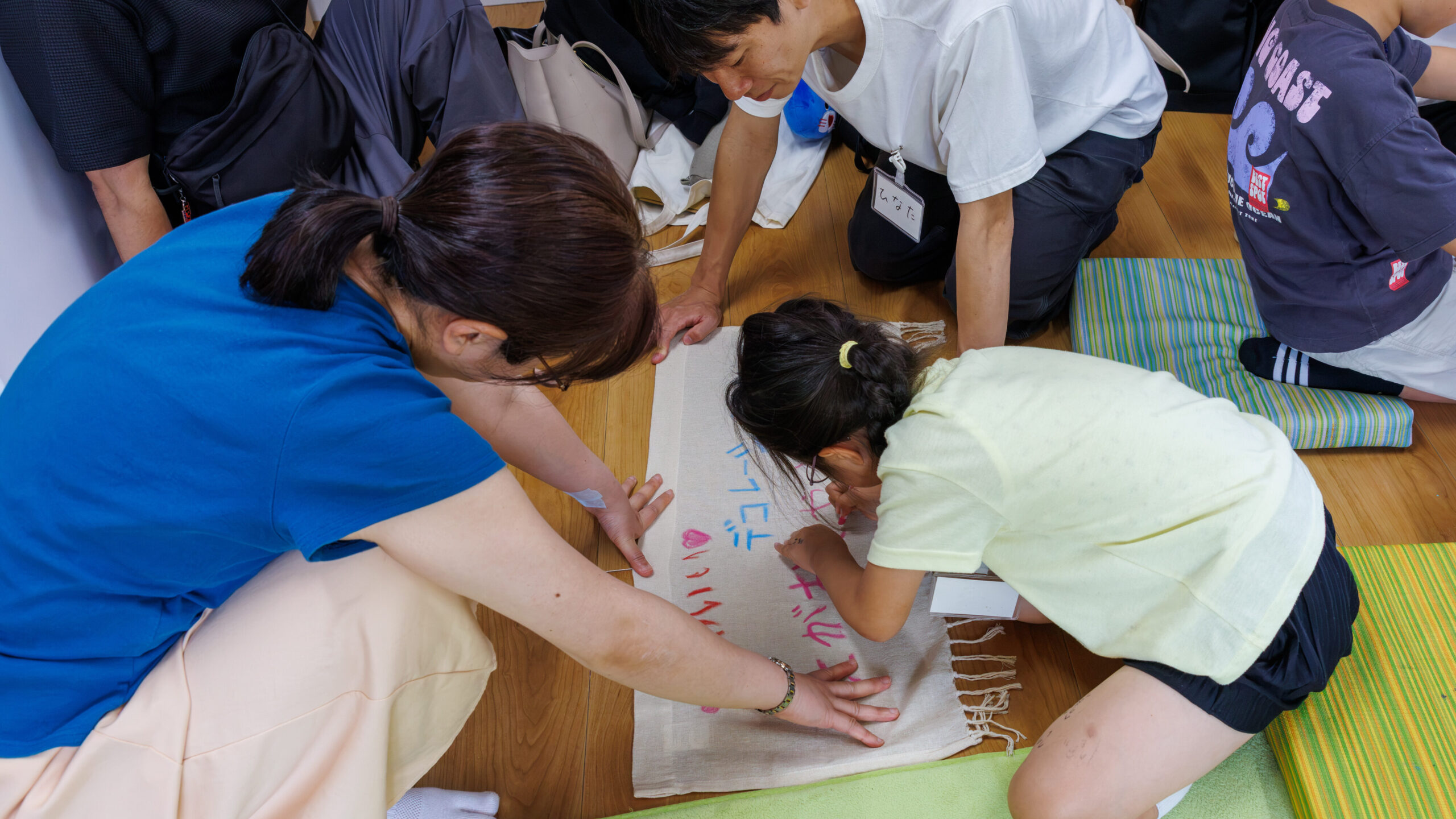 子ども店長プロジェクトでお店の看板になる布に文字やイラストを書き込む子どもとスタッフ
