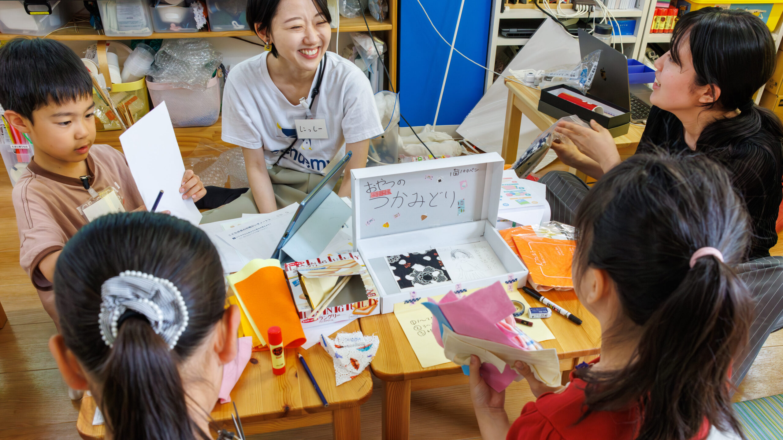 おやつのつかみどりゲームの箱を作りながらスタッフと相談する子ども店長プロジェクトの小学生たち