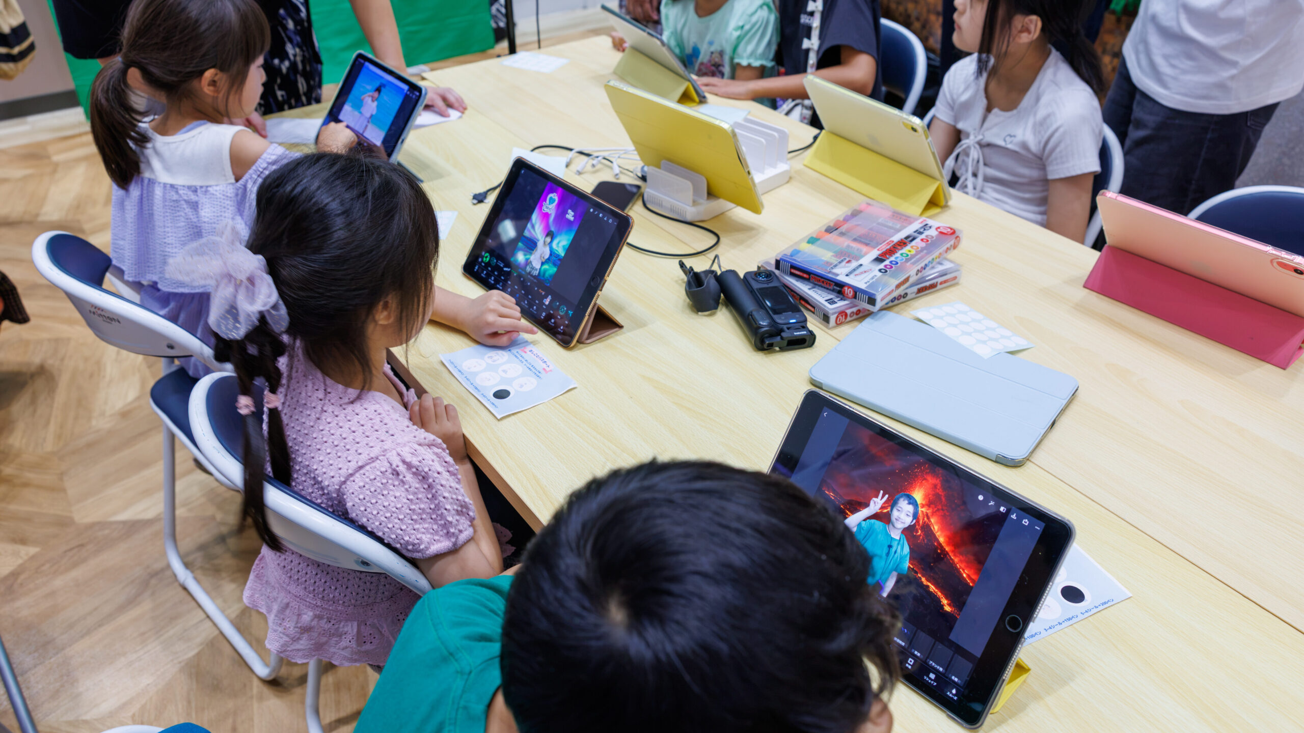 子ども店長プロジェクトのおしごと体験エリアでグリーンバック合成写真をiPadで編集する小学生たち