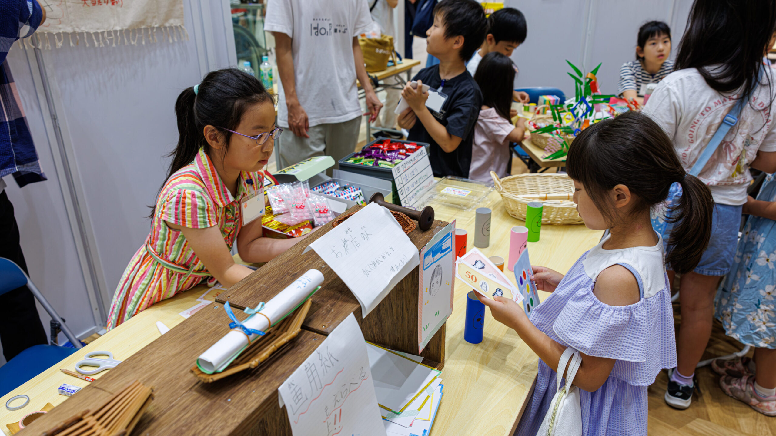 似顔絵屋さんのレジで手作りのお金を受け取り接客する子ども店長プロジェクトの小学生