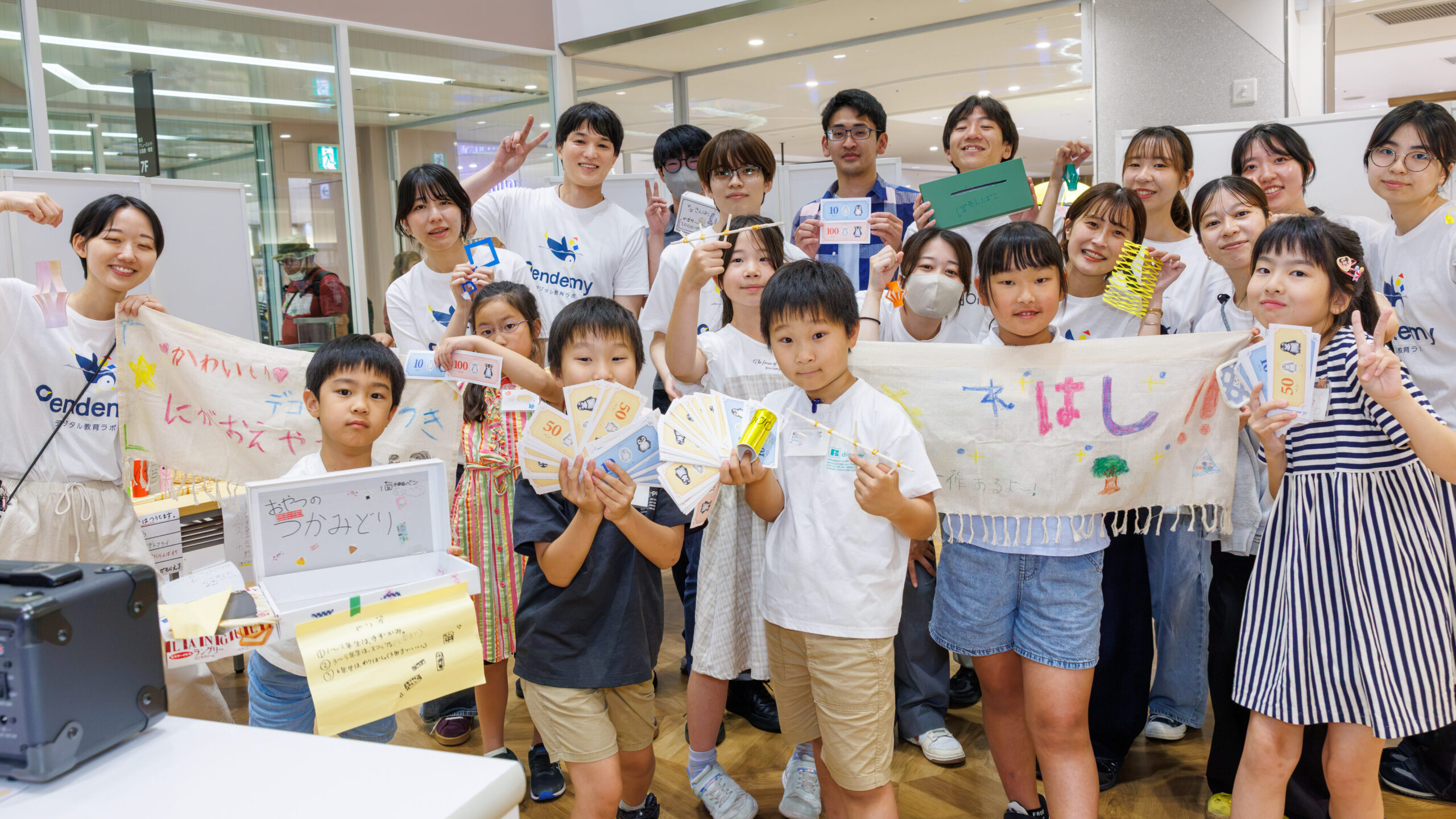 NPO法人Pendemyデジタル教育ラボの経済体験ワークショップで手作りのお金を持つ子どもたちとスタッフの集合写真