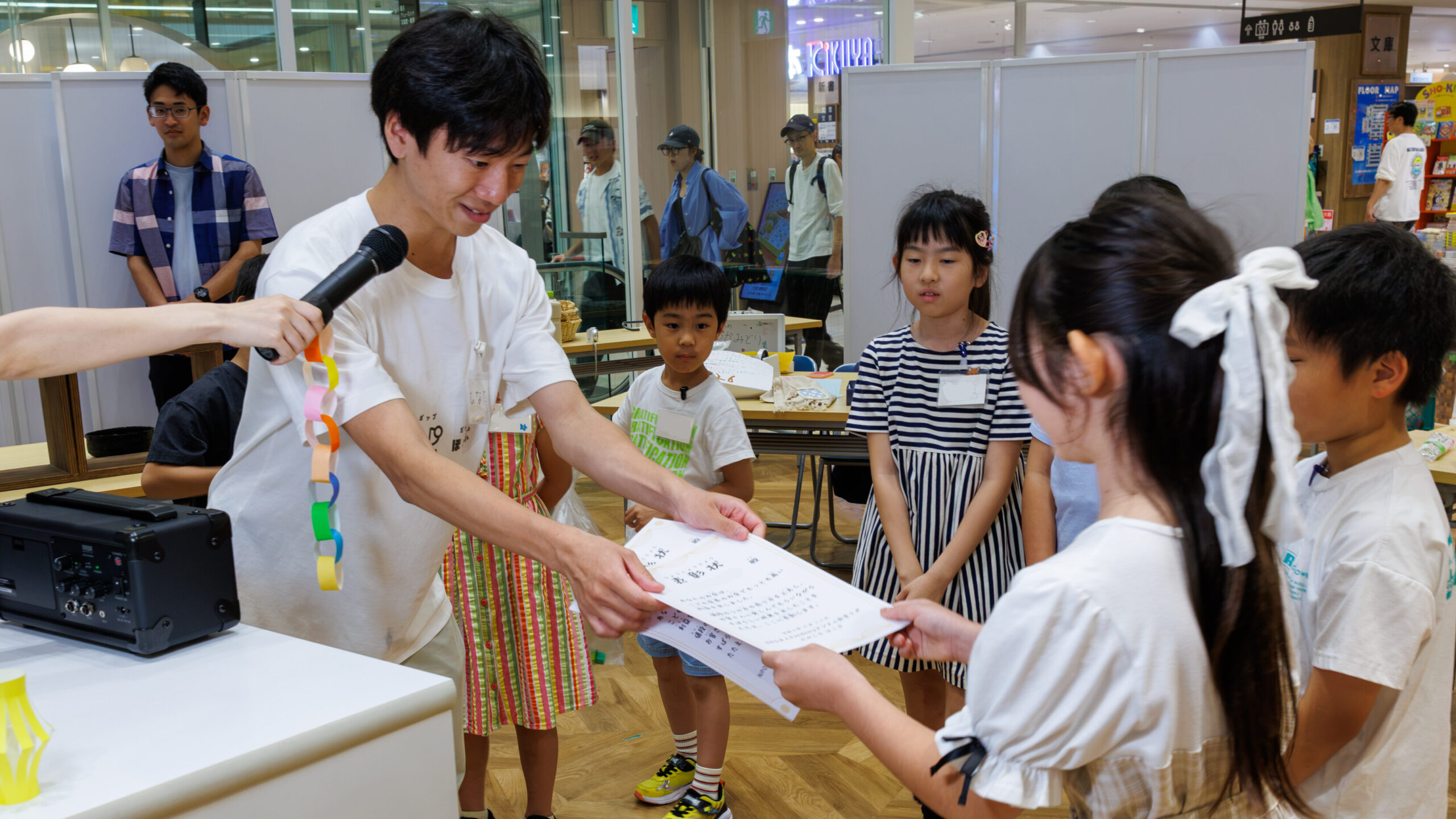 ミッテン府中で開催した子ども店長プロジェクトの表彰式で売上1位のお店に賞状を手渡すスタッフ