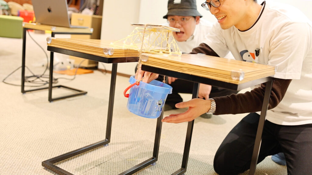 乾燥パスタで組んだトラス構造の橋の耐久テストを行う様子