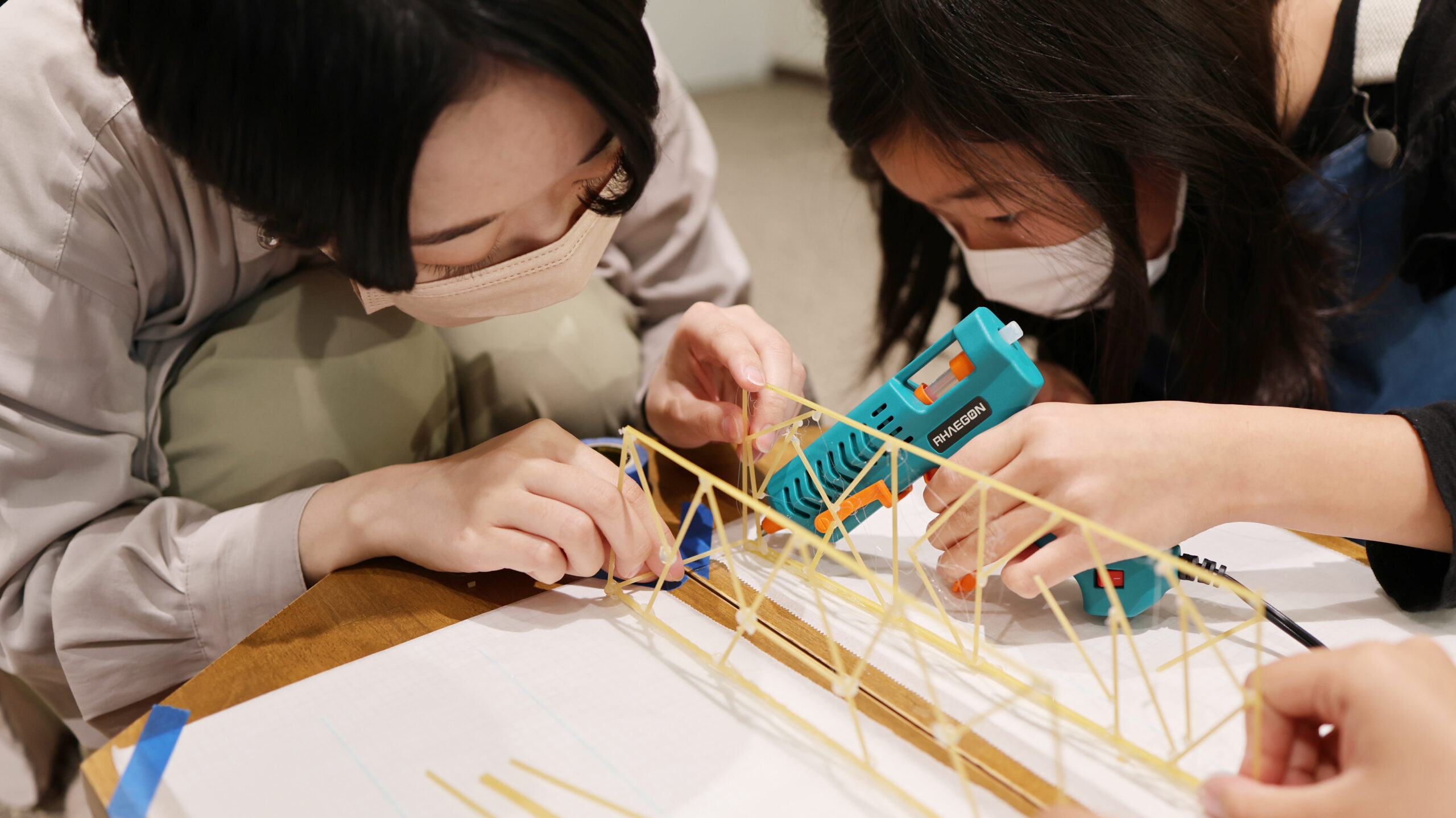 乾燥パスタで組んだトラス構造の橋を、グルーガンを使って組み立てる参加者たち