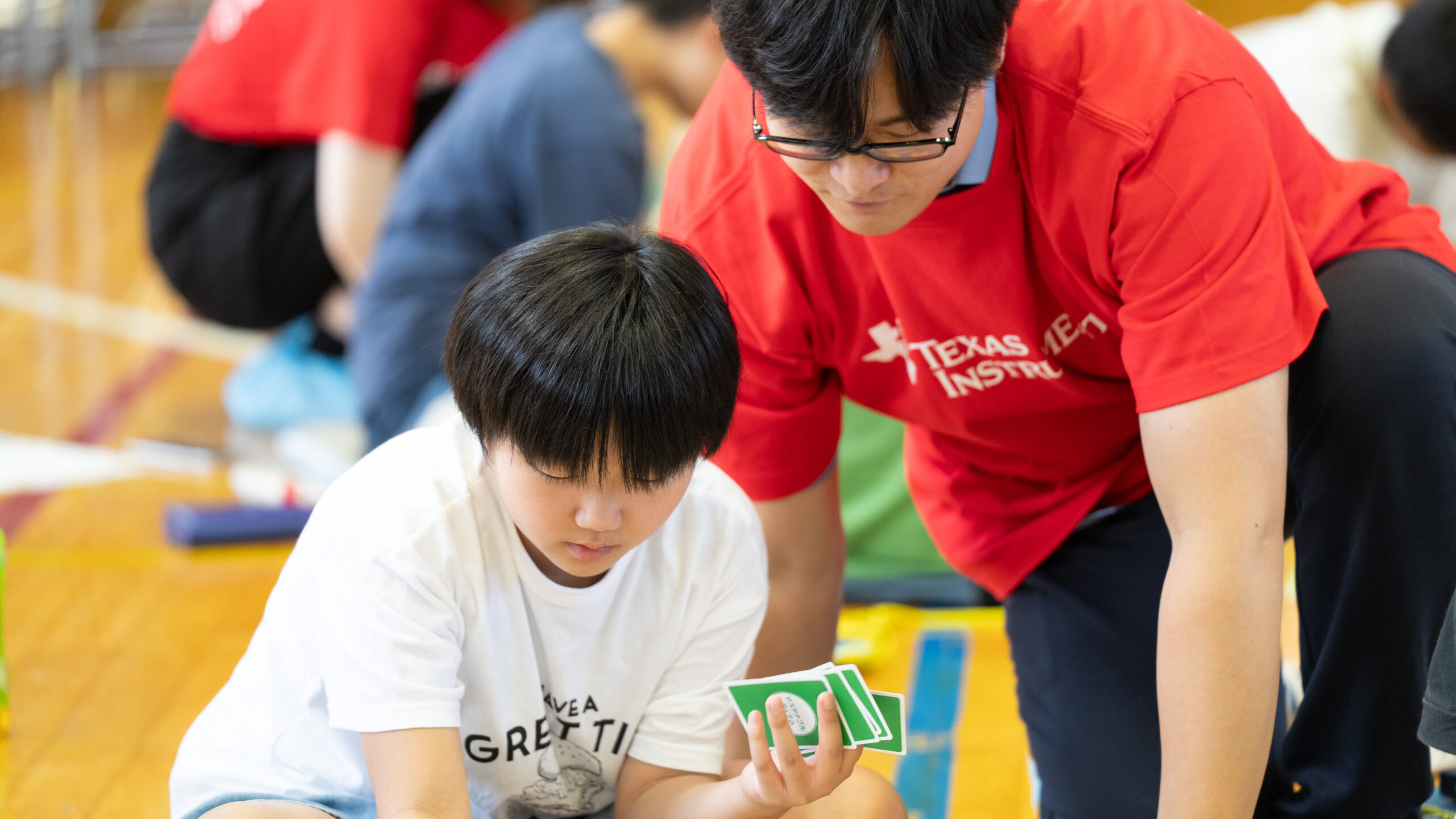 ワークシートに置いたカードを見ながらTI社員と話し合う小学生