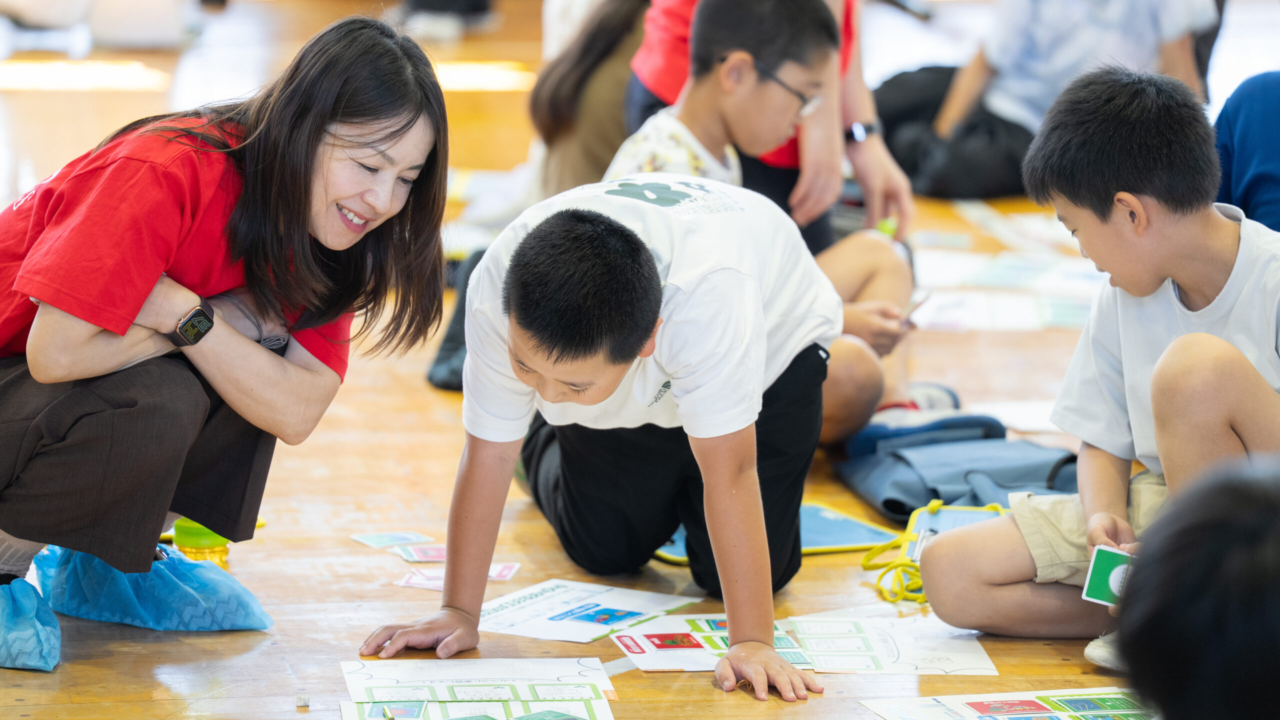 宮前小学校の体育館でTI社員と小学生がグループになってワークシートに取り組む様子
