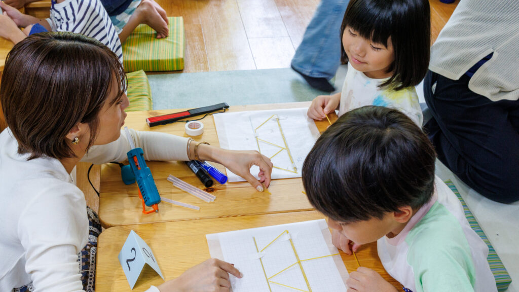 台紙の上に三角形を並べた橋の片面を組み立てる子どもたちとスタッフ